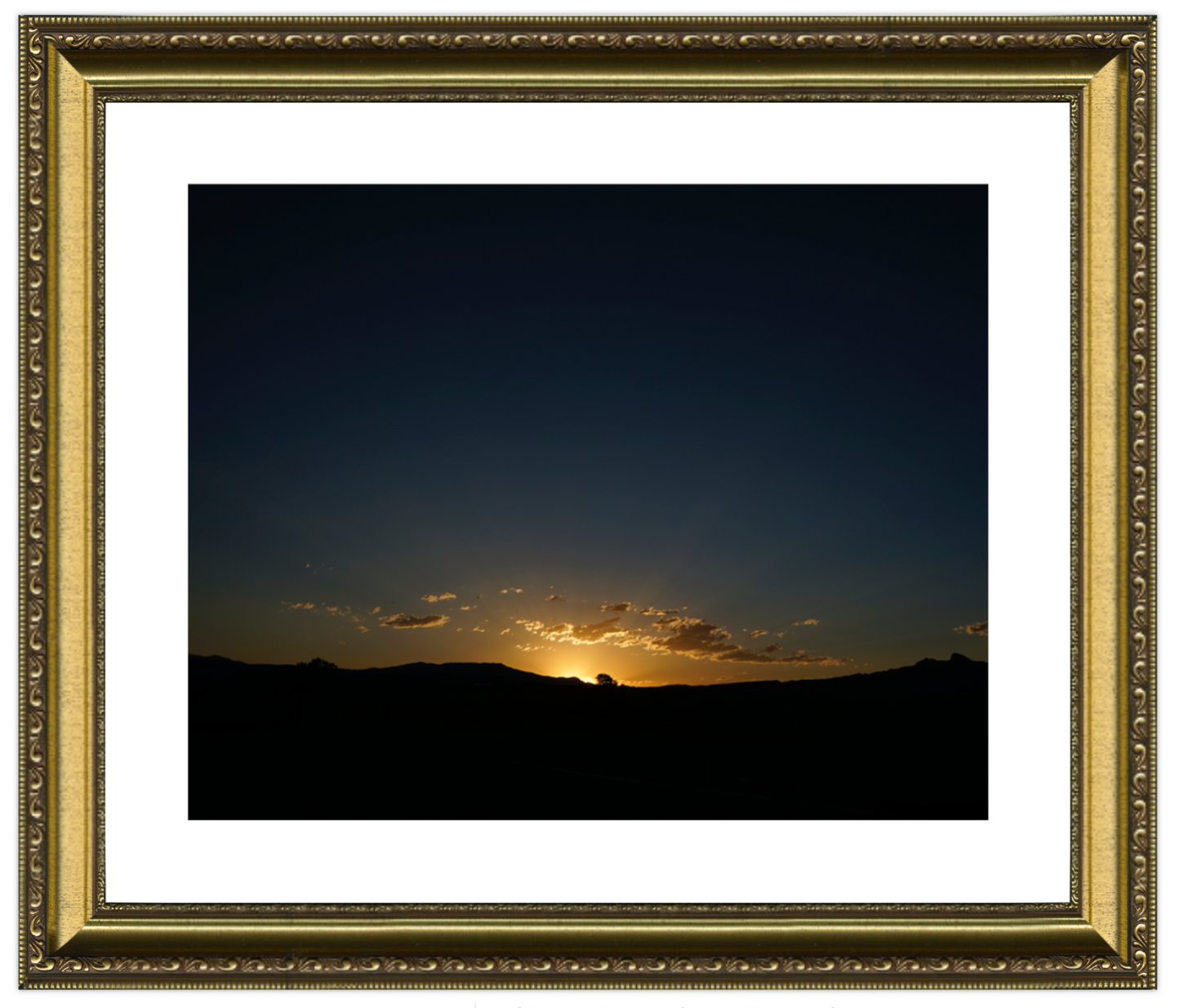 Framed photograph of a sunset over a landscape with a gold frame.