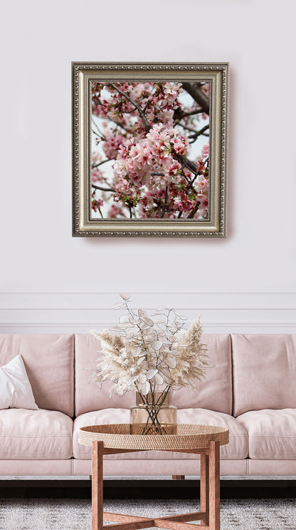 Framed artwork of cherry blossoms above a pink sofa with a small table and flowers.