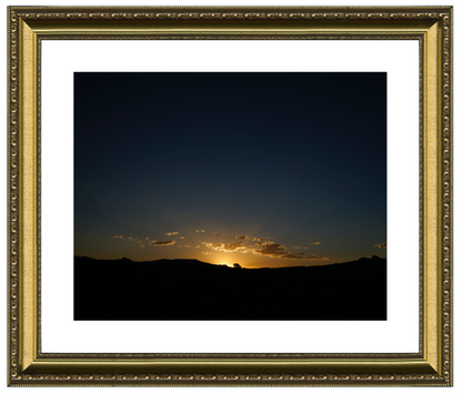Framed photograph of a sunset over a landscape with a gold frame.