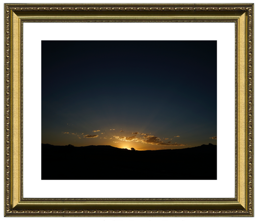 Framed photograph of a sunset over a landscape with a gold frame.
