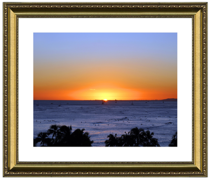 Sunset over the ocean with palm trees in the foreground, framed in gold.