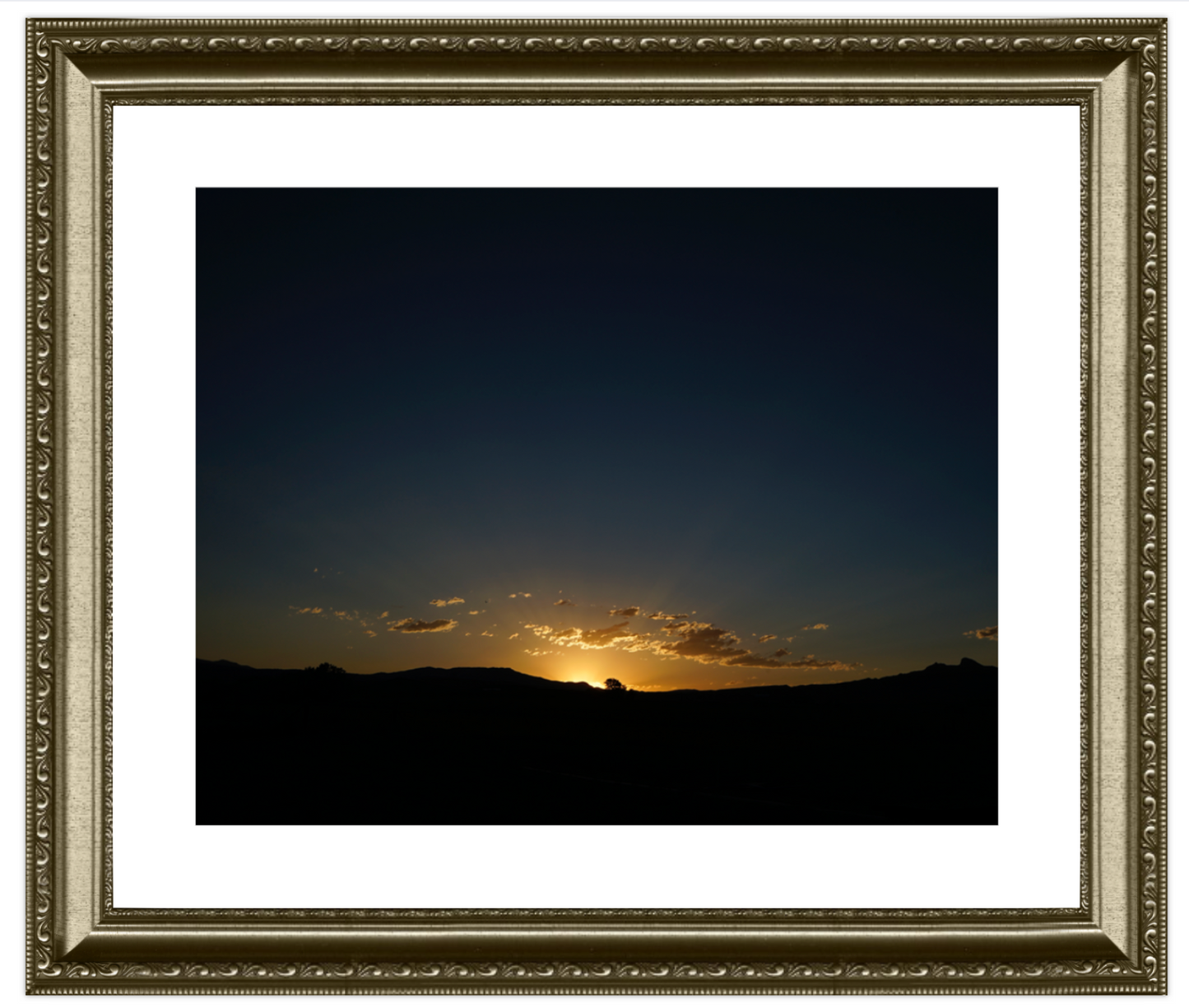 Framed photograph of a sunset over a landscape with a decorative gold frame.