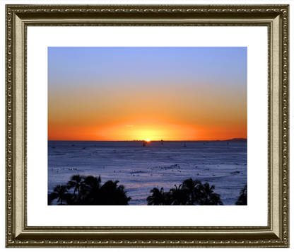 Framed artwork of a sunset over the ocean with palm trees.