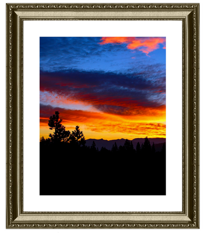 Framed photograph of a sunset over a mountain range with silhouetted trees.