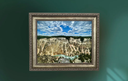 Framed landscape painting of a canyon with a blue sky on a green wall.
