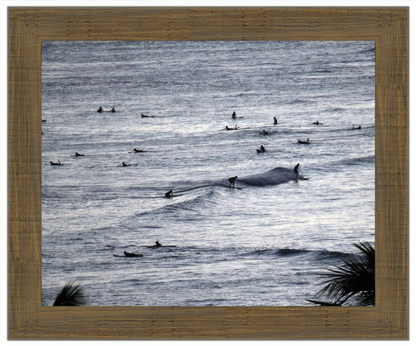Framed artwork of ocean with surfers, framed in brown wood.