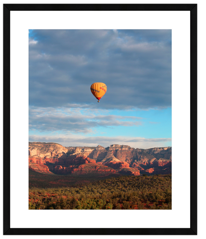 Hot air balloon floating above a desert landscape with mountains in the background