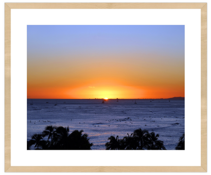 Sunset over the ocean with palm trees in the foreground, framed in beige.