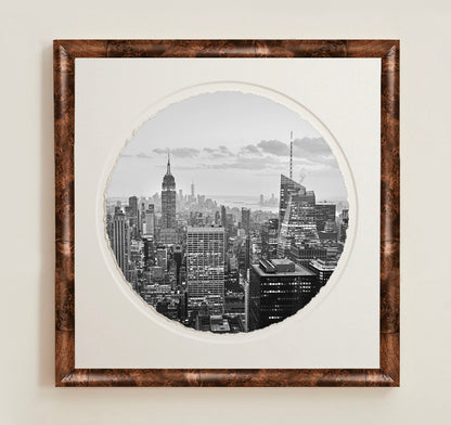 Framed black and white cityscape print on a plain wall.A collection of framed artwork prints with a deckled edge appearance, displayed in two museum style frames named Light Burlwood and Dark Burlwood. The frames are pictured in various sizes with a white mat and clear acrylic front.